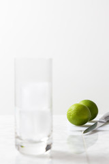 Glass with ice cubes, a knife and two limes. Gin tonic preparation on white background