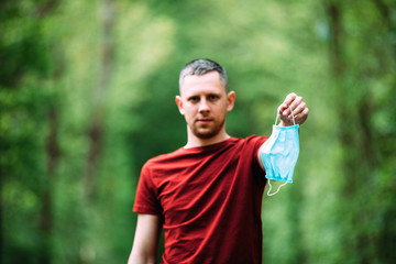 A man holds a medical mask in his hand before forest walking in quarantine period