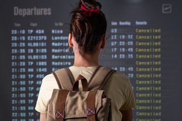 young tourist looking cancelled flights in departure screens at airport - obrazy, fototapety, plakaty