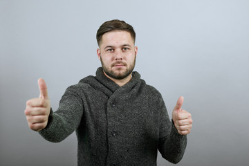 Young Bearded Dark Haired Man In Black Stylish Shirt On Gray Background, Serious Male Holds Thumb Finger Up, Looks Straight Ahead. The Concept Of Cool People, Leaders © Petro