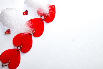 red hearts in the form of a chain and two white bird feathers lie on a white background