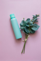 A close-up view of an aquamarine aluminum jar of perfume spray deodorant with a green plant. Green metal bottle flat lay on a pink background. An aerosol can image. A cosmetic bottle for beauty needs.