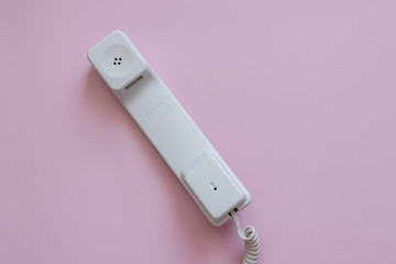 A close up view of A white vintage dial telephone handset on pink background. A retro receiver with phone curly wire and copy space. Office context. Call center. Communication device.