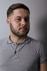 Obraz premium Young Bearded Dark Haired Man In Gray Stylish T-Shirt On Background, Portrait Of A Serious Male Who Looks Away. Close Up