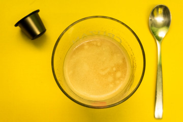 Coffee cup with a spoon and brown capsule on a yellow Surface / Vaso de café con una cuchara y capsula marrón sobre una superficie amarilla