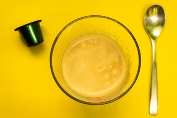 Coffee cup with a spoon and green capsule on a yellow Surface / Vaso de café con una cuchara y capsula verde sobre una superficie amarilla