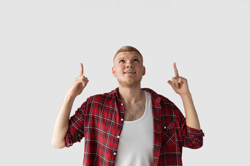 Happy cheerful handsome adult man raising head up, looking and pointing fingers at top...