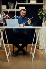 Young innovative caucasian bearded employee sitting in his office and holding windmill model. Sustainable development concept.