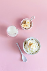 Rice milk porridge with banana slices, daughter and milk on a pink background, top view, flat lay. Vertical
