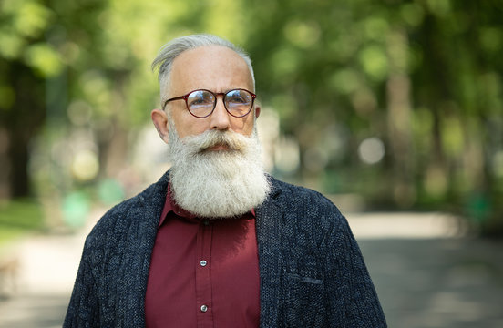 Content Senior Man With A Beard And Wearing Glasses Outdoor.