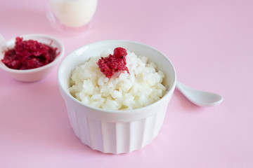 Milk rice pudding with frozen berries on a pink background