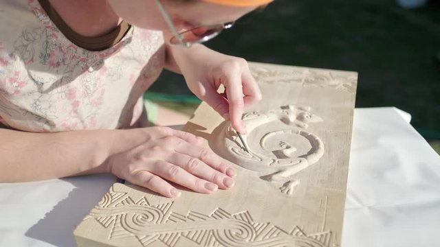 Artist working with wood. Woman carves wooden plank and creates animal (gekko) on it and makes polishing work
