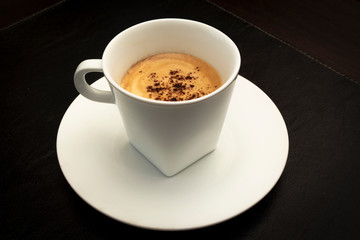 top view of white cup of coffee on a dark black background.