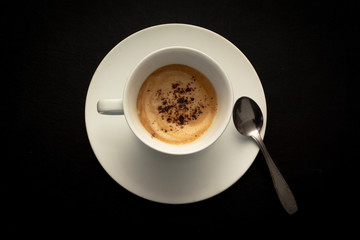 top view of white cup of coffee on a dark black background.