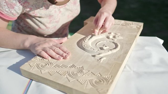Artist working with wood. Woman carves wooden plank and creates animal (gekko) on it and makes polishing work