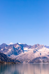 Alaska Cruise to Glacier Bay national park, scenic view of snow capped mountains at sunset from the ship. Sunny weather, sea, snowy cliffs and hills, a clear blue sky. Inside Passage of Alaska.