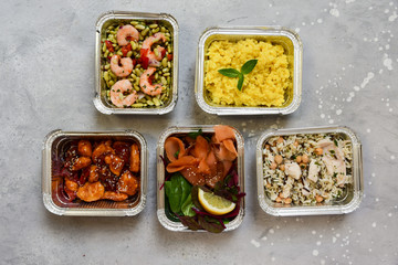 Food delivery. Different aluminium lunch box with healthy natural food risotto, chicken chickpeas and rice, salmon salad, hot chicken teriyaki, shrimp and green beans. airlines food. airline meals