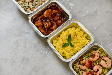 Food delivery. Different aluminium lunch box with healthy natural food risotto, chicken chickpeas and rice, salmon salad, hot chicken teriyaki, shrimp and green beans. airlines food. airline meals