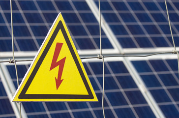 Solar power farm station on a background selective focus on a yellow triangular high voltage warning sign. The inscription in Russian "Do not come near kill"