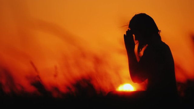 Profile of a woman in prayer at sunset
