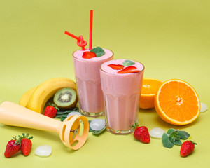 two glasses of cocktail with mint and strawberries on top. around different fruits and ice (banana, orange, kiwi, strawberries)