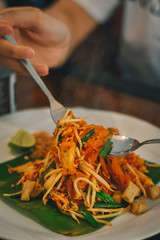 close up of a woman holding a bowl of Pad Thai, stir-fried rice noodles.