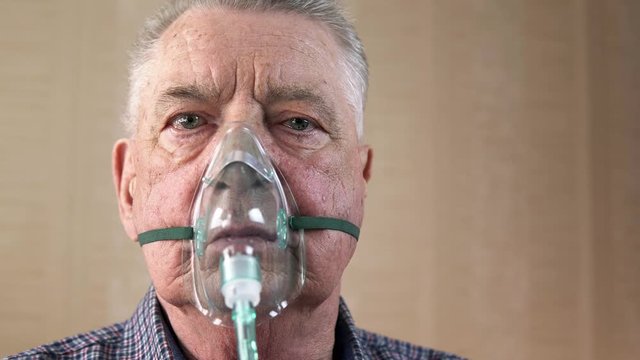 Portrait of an elderly man with COPD in an oxygen mask who is breathing deeply. Theme of a serious and incurable disease of lungs and respiratory system. Grandfather breathes in a special medical mask
