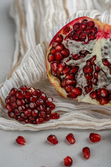 Half of pomegranate and pomegranate seeds are laying on beige textile