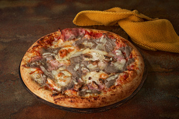 Homemade pizza with mushroom sauce, ham, mushrooms, tomato paste over dark surface, selective focus.