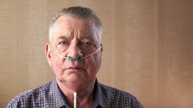 Portrait of an old man with a medical nasal oxygen catheter deep breathing. Theme of a serious and incurable disease of lungs and respiratory system. Grandfather breathes in a special medical mask