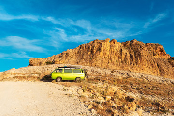 Vintage camper van parked on the slopes of rocky arid desert land.