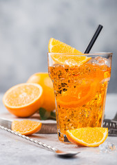 Aperol spritz summer cocktail in highball glass with oranges and bar spoon on light background. Ice cubes and black straw.