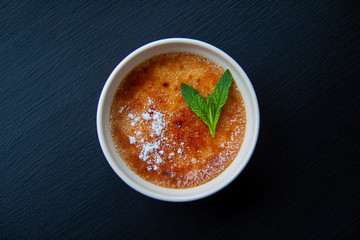 Dessert creme brulee with a sprig of mint sprinkled with icing sugar.  Dessert on a black gradient background