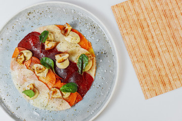 carpaccio of vegetables sprinkled with mushrooms on a white plate next to the menu