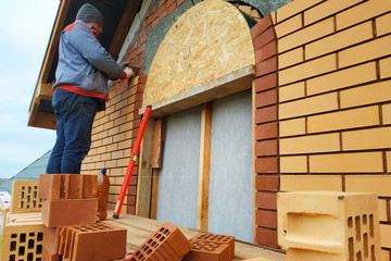 Fototapeta premium The master in a blue overalls builds a wall of face brick.