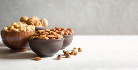Hazelnuts, cashews, almonds and walnuts. Nuts in wooden and clay bowls on a gray background with a...