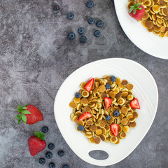 Pancake cereal. Trendy food, mini cereal pancakes in bowl on the table, grey cement background. Trendy baked mini pancakes with strawberries, blueberries . Copy space. Flat layout. Table top view.