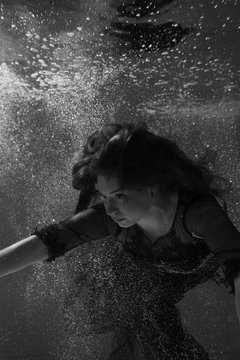 Black and white photo. Beautiful girl underwater in a red dress swims in the pool. Tenderness and elegance. Bubbles and a lot of water