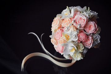 Elegant wedding bouquet in white and pink pastel colors with silk ribbons on a black background. Classic earrings with precious stones and pearls on roses and orchids.