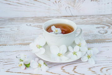 White cup of tea and apple blossom on white paint wooden background