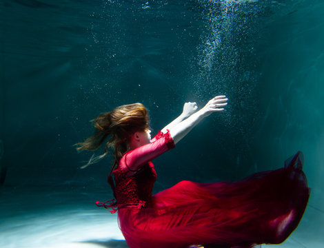 Beautiful girl underwater in a red dress swims in the pool. Tenderness and elegance. Bubbles and a lot of water