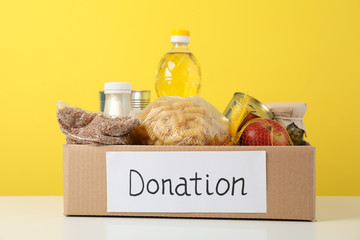 Donation box with different food against yellow background. Volunteering