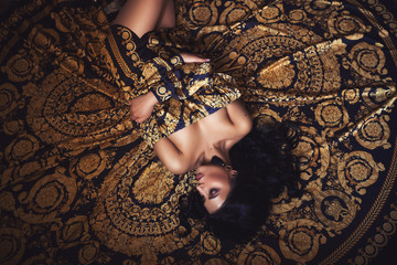 Portrait of a beautiful tanned brunette girl in a silk black and gold dress