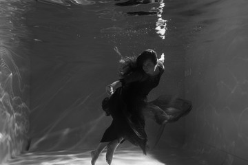 Fototapeta na wymiar Black and white photo. Beautiful girl underwater in a red dress swims in the pool. Tenderness and elegance. Bubbles and a lot of water