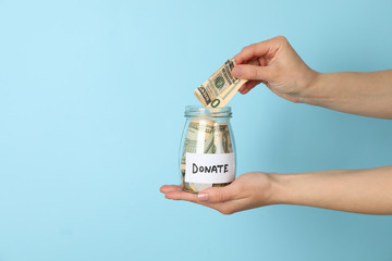 Female hand puts money in glass jar on blue  background