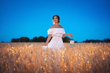 Romantic portrait of a girl in a white summer dress in a field of wheat at night