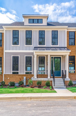 Modern townhouse with horizontal, vertical light gray vinyl siding , square black frame windows, covered porch with white columns curb side appeal on a new construction neighborhood street in Maryland