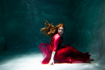 Beautiful girl underwater in a red dress swims in the pool. Tenderness and elegance. Bubbles and a...