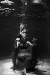 Fototapeta na wymiar Black and white photo. Beautiful girl underwater in a red dress swims in the pool. Tenderness and elegance. Bubbles and a lot of water