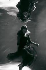 Obraz premium Black and white photo. Beautiful girl underwater in a red dress swims in the pool. Tenderness and elegance. Bubbles and a lot of water